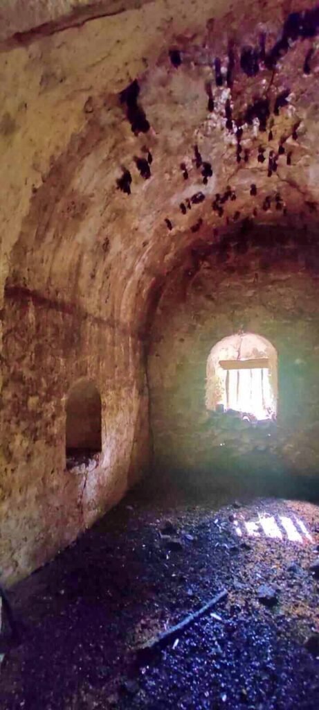 Interior de las ruinas de Boca Iglesia con muros de piedra y luz natural entrando por una ventana.