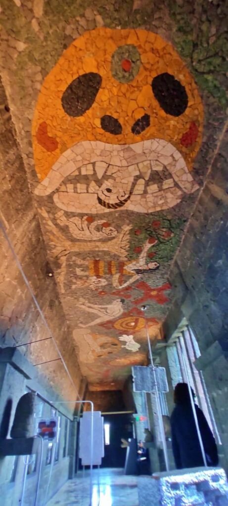 Techo con mosaico y figuras en un pasillo interior del Museo Anahuacalli, con muros de piedra volcánica.
