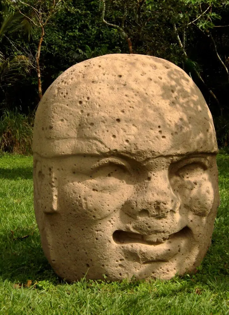 Cabeza colosal olmeca vista lateral con vegetación tropical de fondo