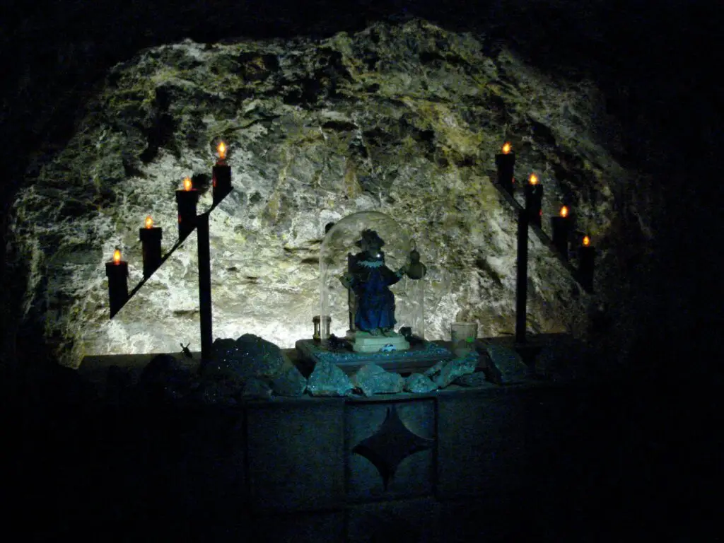 Capilla minera dentro de la Mina del Edén con imagen religiosa protegida por urna y veladoras encendidas.