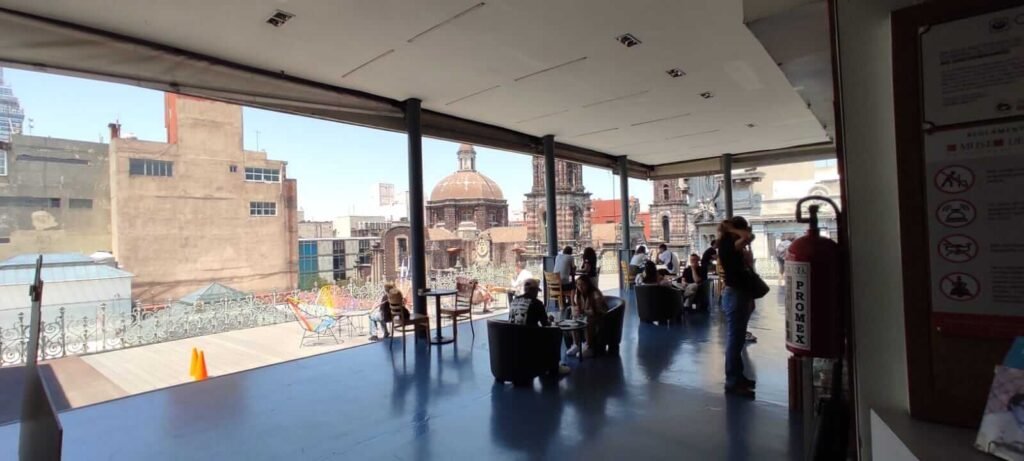 Terraza con visitantes sentados y vista urbana de CDMX al fondo, desde el Museo del Estanquillo.