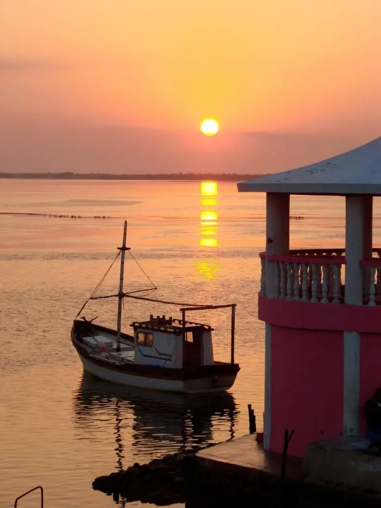 Amanecer sobre el mar con lancha pesquera junto a muelle y estructura rosa.