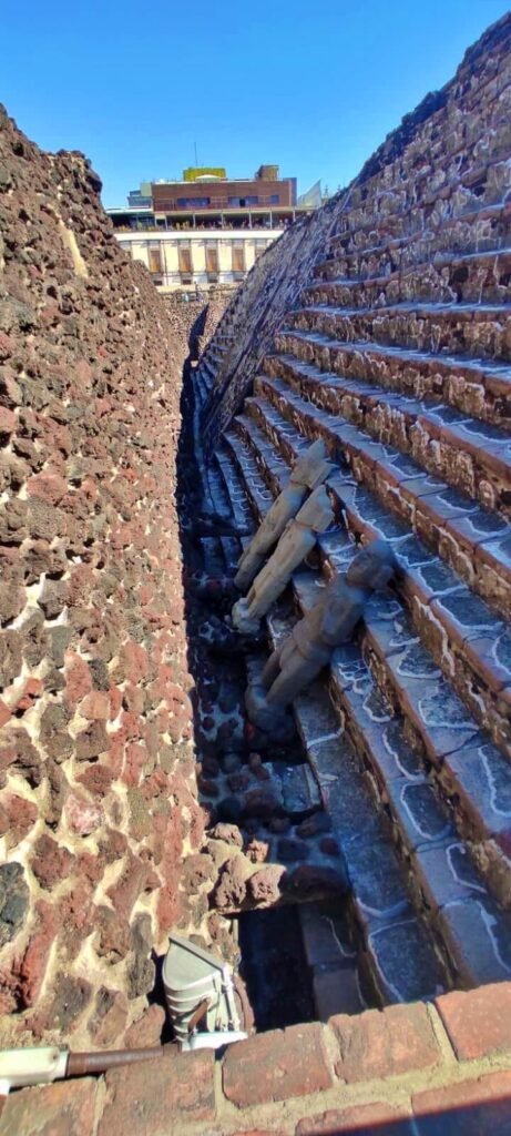Pasaje de piedra entre muros y escalones en la zona arqueológica del Templo Mayor, bajo cielo azul, CDMX.