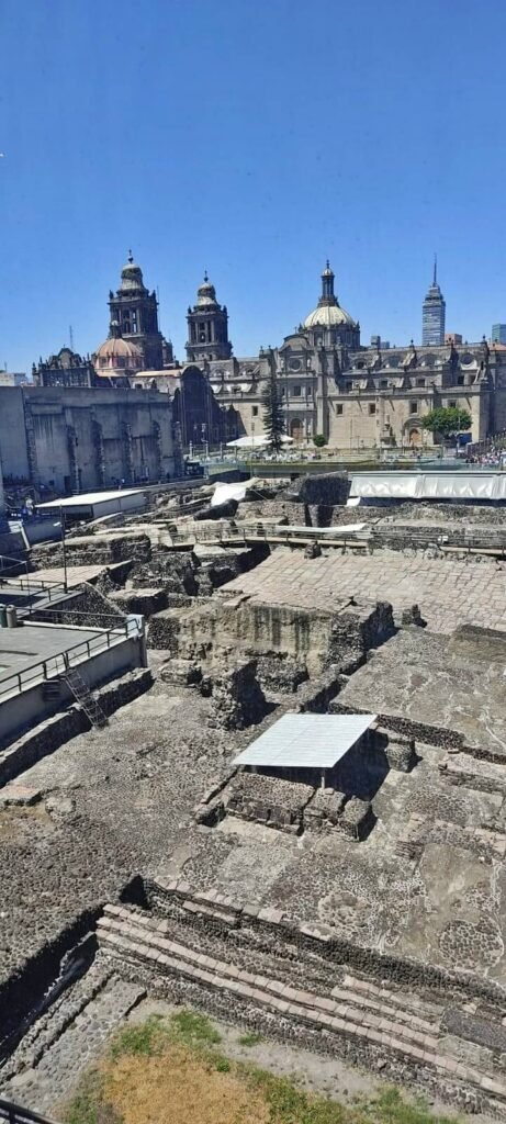 Panorámica del Templo Mayor con ruinas y la Catedral Metropolitana al fondo bajo cielo azul, Centro Histórico de CDMX.