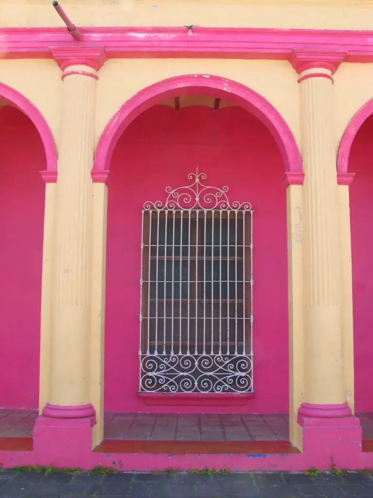 Fachada tradicional de Tlacotalpan con arcos coloniales pintados en rosa y amarillo, columnas simétricas y ventana con herrería.