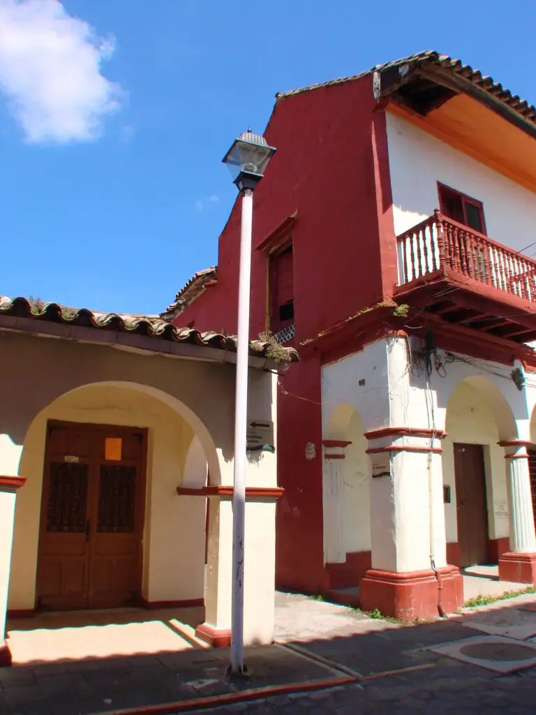 Fachada colonial de Tlacotalpan con columnas amarillas, muros rosas y ventana con reja decorativa de hierro.