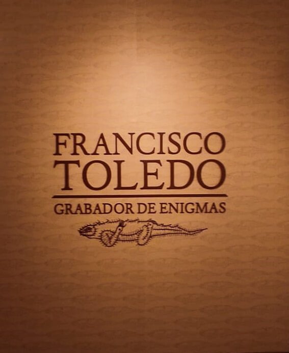 Texto en pared que dice “Francisco Toledo, grabador de enigmas” con un dibujo debajo.