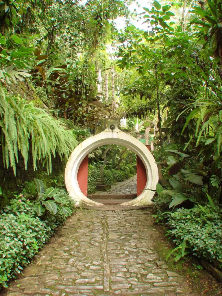 Portal circular blanco enmarcando un sendero empedrado entre plantas exuberantes del Jardín Surrealista de Xilitla.