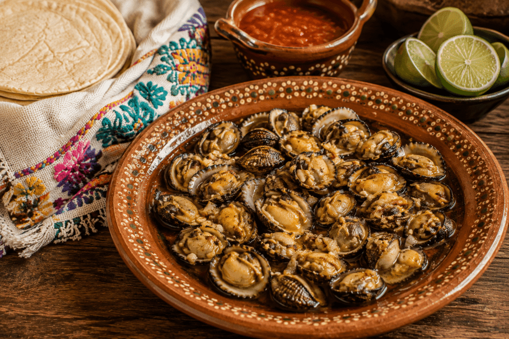 Tichindas al mojo de ajo servidas en plato de barro, acompañadas de tortillas de maíz, salsa roja y limones, platillo tradicional de la Costa de Oaxaca.